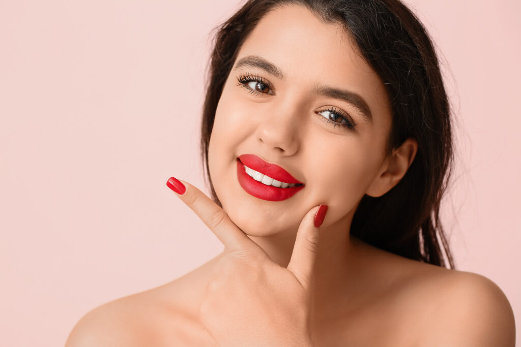 Smiling young woman with red lipstick against pink background, closeup