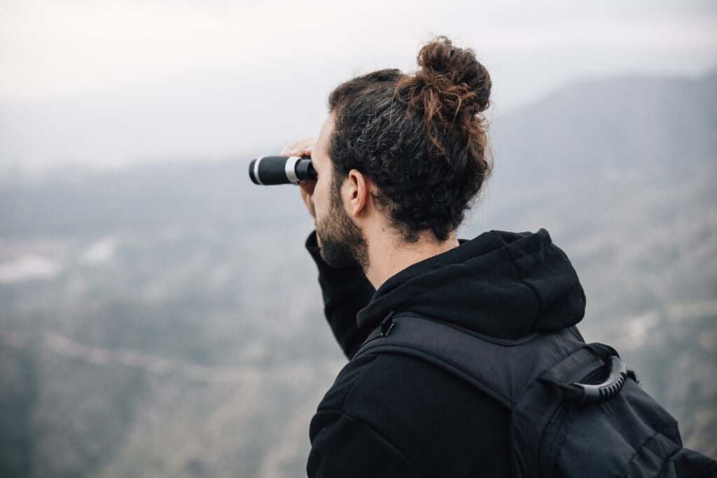 male hiker with his backpack looking mountain view through binocular