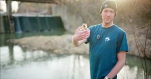 Mężczyzna trzyma głowę martwej ryby w dłoni nad rzeką Mleczką.