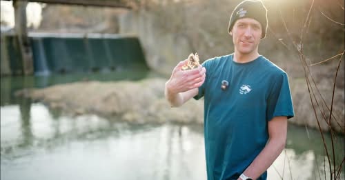 Mężczyzna trzyma głowę martwej ryby w dłoni nad rzeką Mleczką.